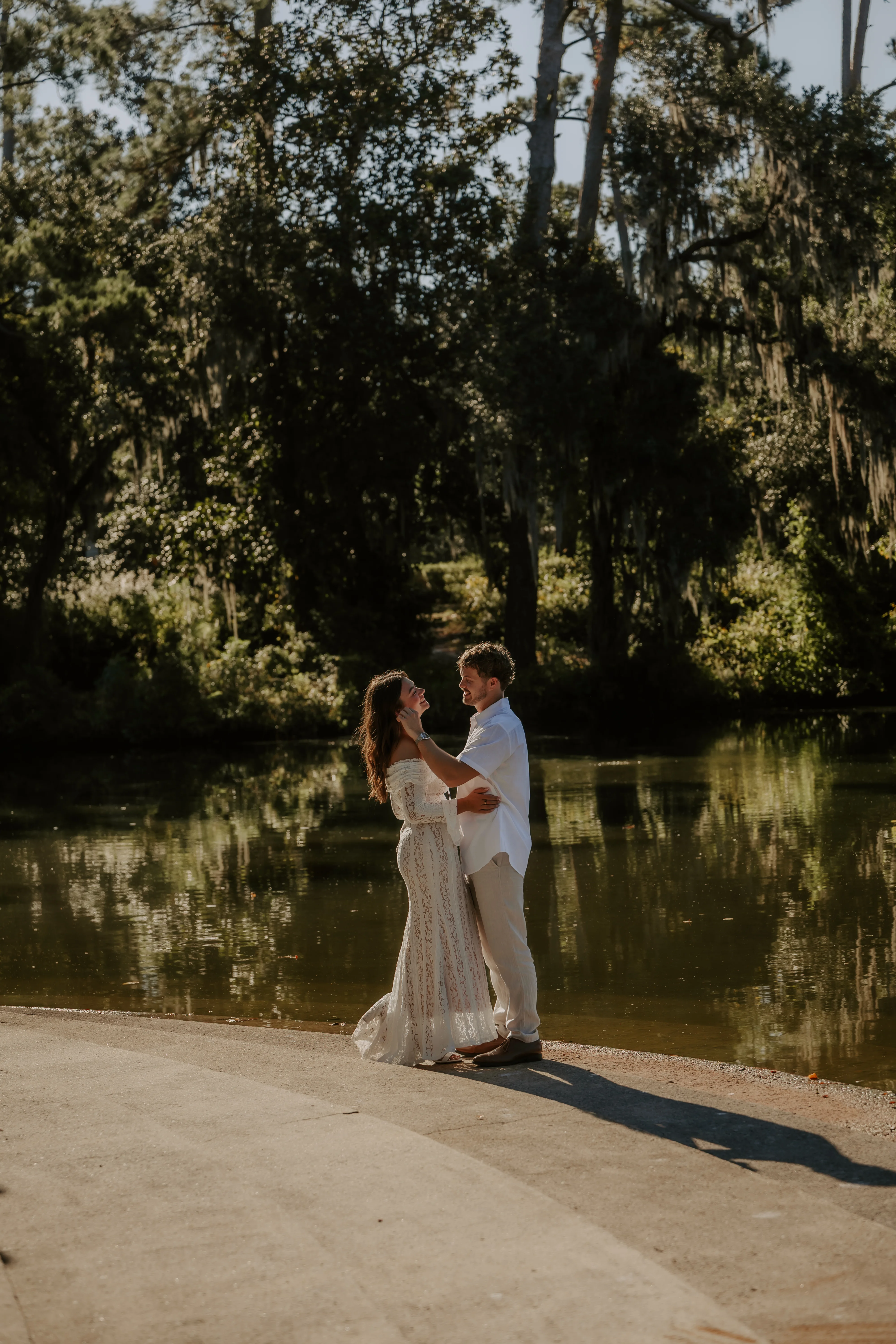 The couple embracing at the water's edge beneath moss-draped trees